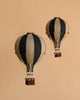 Two vintage-style Hot Air Balloon - Black models with black and beige stripes and small woven baskets float against a plain beige background—ideal as unique children's room decor.