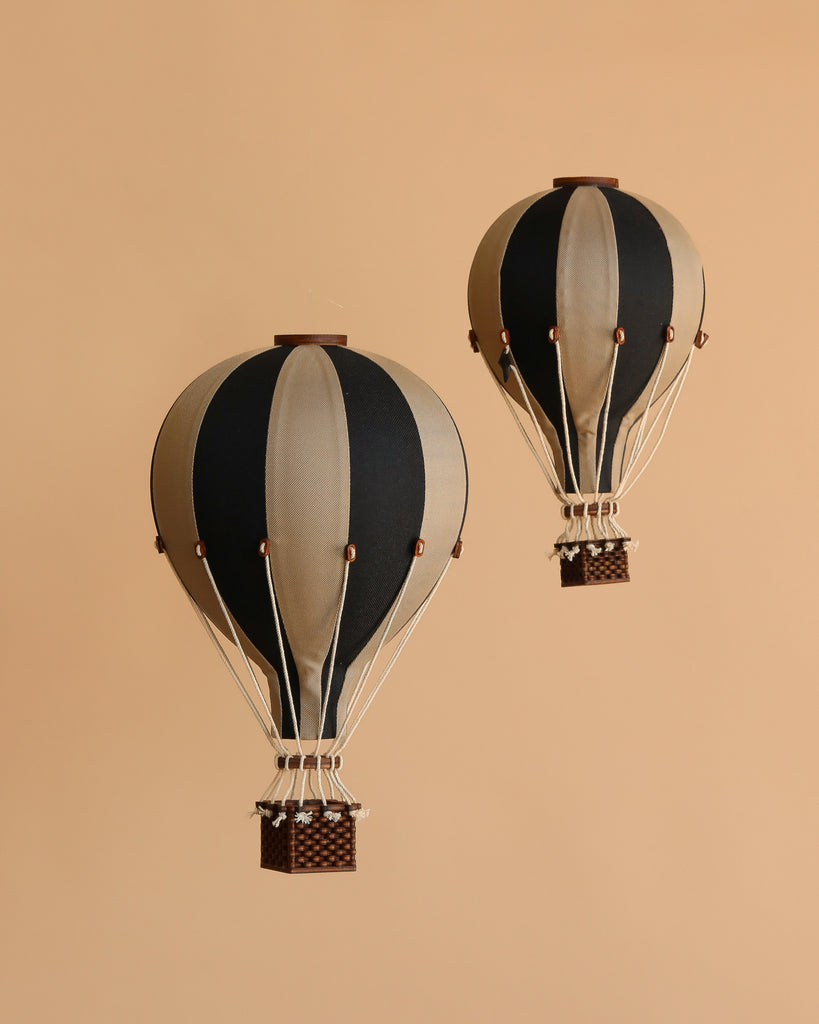 Two vintage-style Hot Air Balloon - Black models with black and beige stripes and small woven baskets float against a plain beige background—ideal as unique children's room decor.