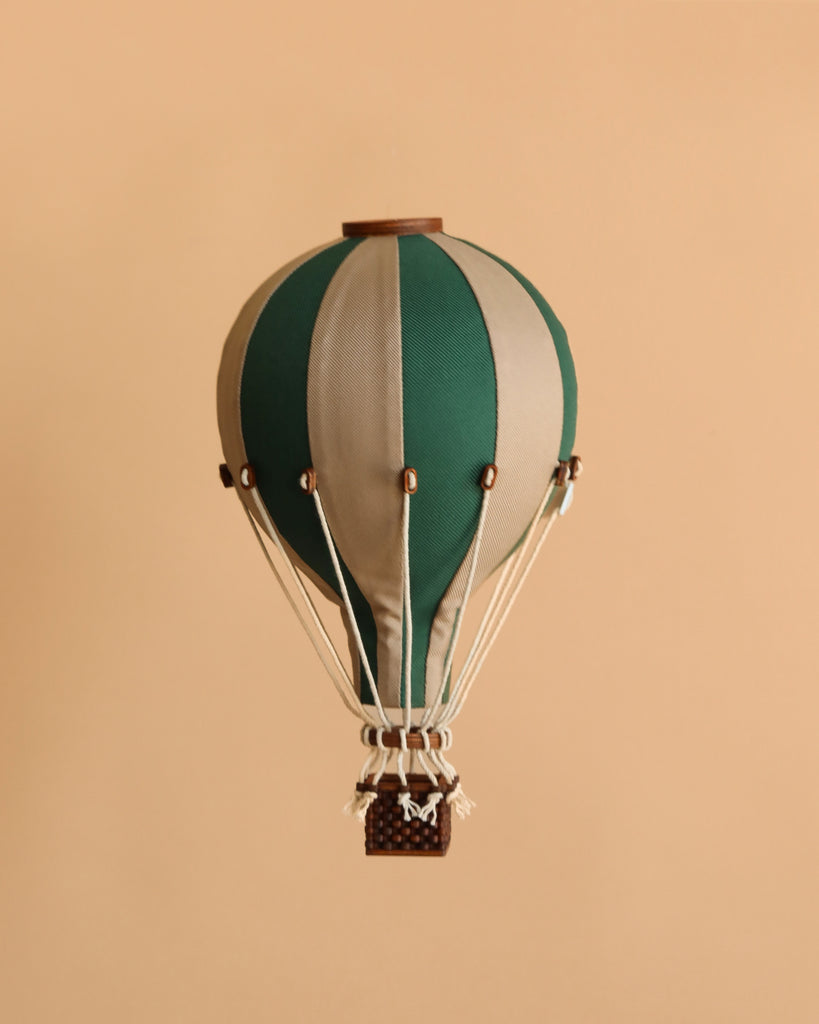 The Hot Air Balloon - Light Brown / Green is a small, handmade model featuring green and beige stripes and a woven basket—ideal as a charming decoration for a child’s room.