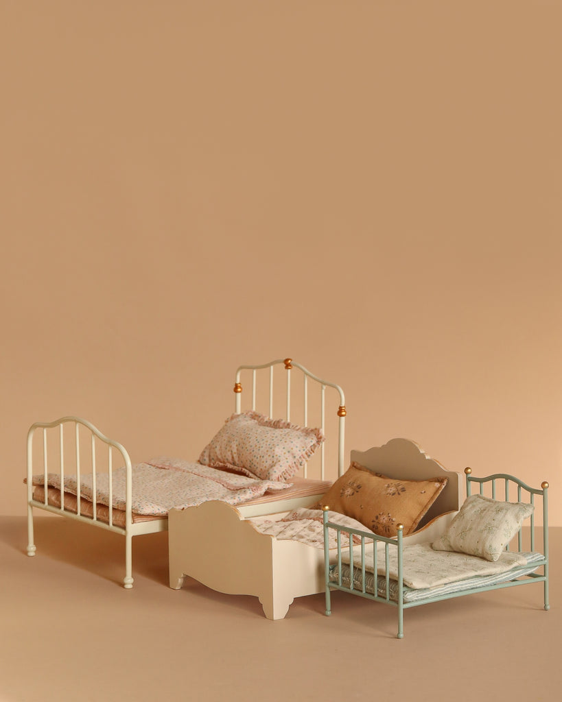 The Maileg Vintage Bed, Mouse Size - Off White, features a charming vintage-style frame and patterned bedding, perfect for dollhouse displays. Shown arranged on a beige surface with coordinating background for added appeal.