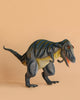 The Giganotosaurus Dinosaur Stuffed Animal, featuring blue stripes and a yellowish underbelly, stands on a plain peach background with its mouth open in a roaring pose.