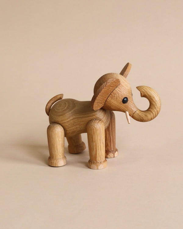 A Spring Copenhagen Ollie - Elephant toy with a prominent trunk and tusks, displayed against a plain beige backdrop. Made from FSC Oak, its body showcases natural wood grain texture.