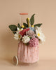 A small peach-colored cart with white polka dots holds a bouquet of handmade fabric flowers. The bouquet includes white daisies, pink and purple roses, red flowers, and green leaves. The Felt Flower Trolley Basket has white wheels and a peach-colored handle against a beige background, showcasing eco-friendly craftsmanship.