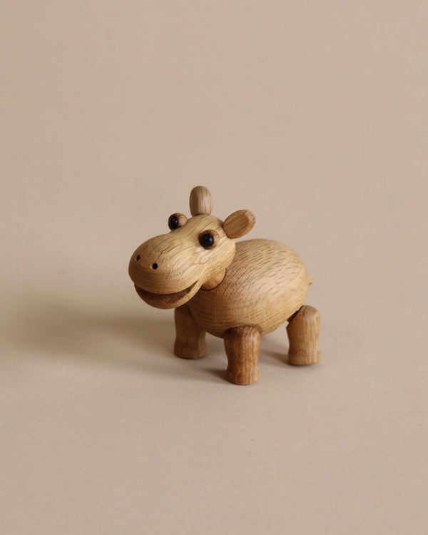 A small wooden toy figurine of a hippopotamus calf with round black eyes stands against a plain beige background. Crafted from FSC Oak, the Spring Copenhagen Wilma has a smooth, polished finish and a friendly, smiling expression that captures the charm of African wildlife.