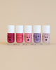 Five bottles of Nailmatic water-based nail polishes with cartoon faces on a beige background, ranging in colors from deep red to soft pink, each showing different facial expressions.