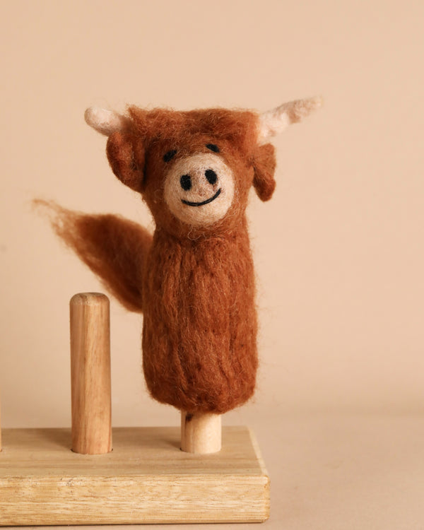 The Highland Cow Finger Puppet, an enchanting handmade toy animal displayed on a wooden stand, brings a unique flair to your finger puppet collection.