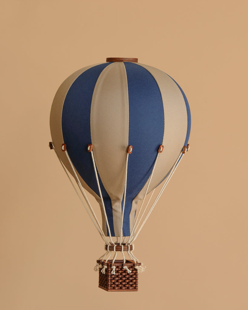 The Hot Air Balloon - Navy Blue features alternating navy blue and beige panels, white ropes, and a brown wicker basket—perfect as a vintage-style handmade children's room decoration against a plain beige background.