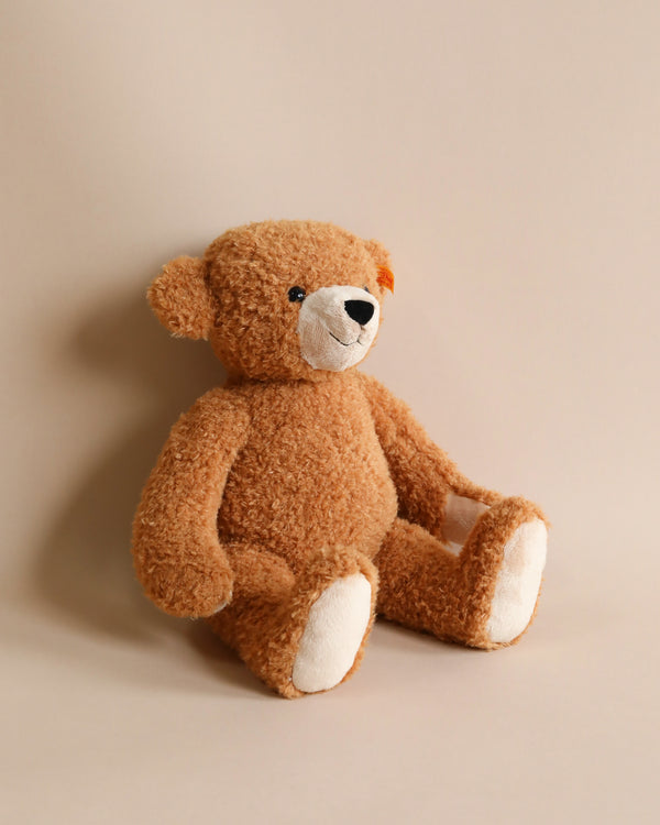 A Steiff Happy Teddy Bear, 16 inches tall, sits against a plain beige background, looking directly at the viewer with its black and white button eyes.