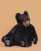 The Brown Tommy Bear Stuffed Animal, 30", features soft dark brown fur, large visible paws, and realistic detailing. It is pictured sitting on a light peach background with its head slightly tilted to the side.