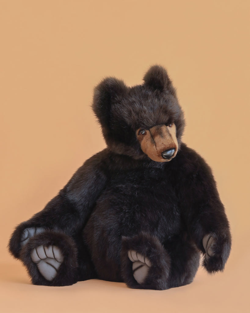 The Brown Tommy Bear Stuffed Animal, 30", features soft dark brown fur, large visible paws, and realistic detailing. It is pictured sitting on a light peach background with its head slightly tilted to the side.