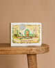 1 Is One by Tasha Tudor" rests on a wooden bench with a plain beige backdrop. Its cover shows a child among flowers and animals, making it an ideal addition to any counting book collection.