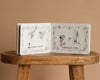 Inspired by Tasha Tudor, "1 Is One" is a classic board book featuring gentle counting moments—like two birds and two girls making a wish—perfect for little readers.