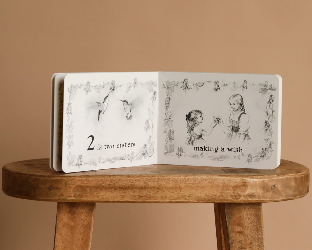 Inspired by Tasha Tudor, "1 Is One" is a classic board book featuring gentle counting moments—like two birds and two girls making a wish—perfect for little readers.