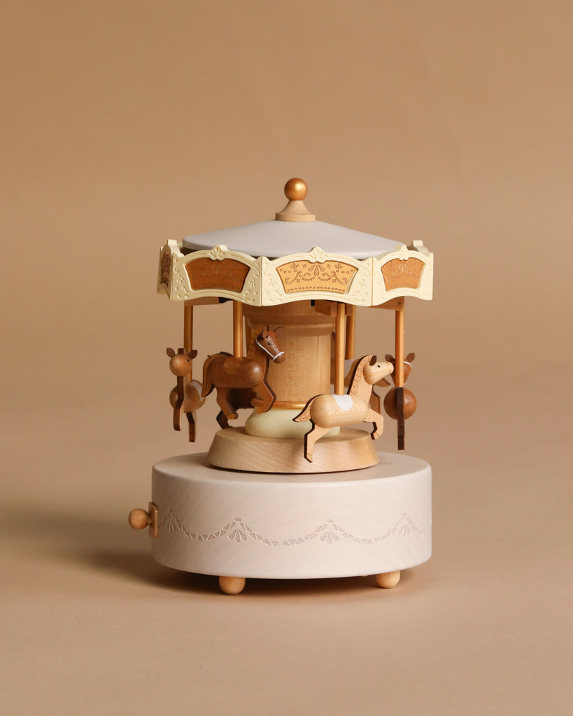 The Wooden Carousel Music Box features horse figurines and a crank handle, designed in a classic carousel style and set against a plain beige background.