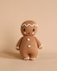 The Cuddle + Kind Baby Gingerbread is a collectible knitted doll made from Peruvian cotton yarn that stands upright. It showcases embroidered eyes and a smile, along with white icing details on its head, arms, and three buttons on its body against a plain beige background.