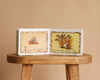 1 Is One by Tasha Tudor is open on a wooden stool, displaying illustrations of apples and someone picking apples. The counting book reads "7 is seven apples" on one page and "on a little apple tree" on the other.