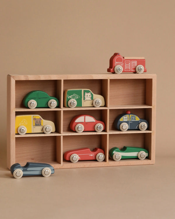 The Konges Sløjd - Wooden Mini Car Set features a beechwood box containing nine vibrant mini cars, each with a unique design and white wheels, all set against a neutral beige background that accentuates the colorful toys.