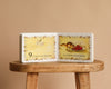 1 Is One by Tasha Tudor is open on a wooden stool. The left page shows the number 9 and cherries, with “9 is nine red cherries.” The right page shows a plate of cherries and the text "on a white china plate." A charming counting book!.