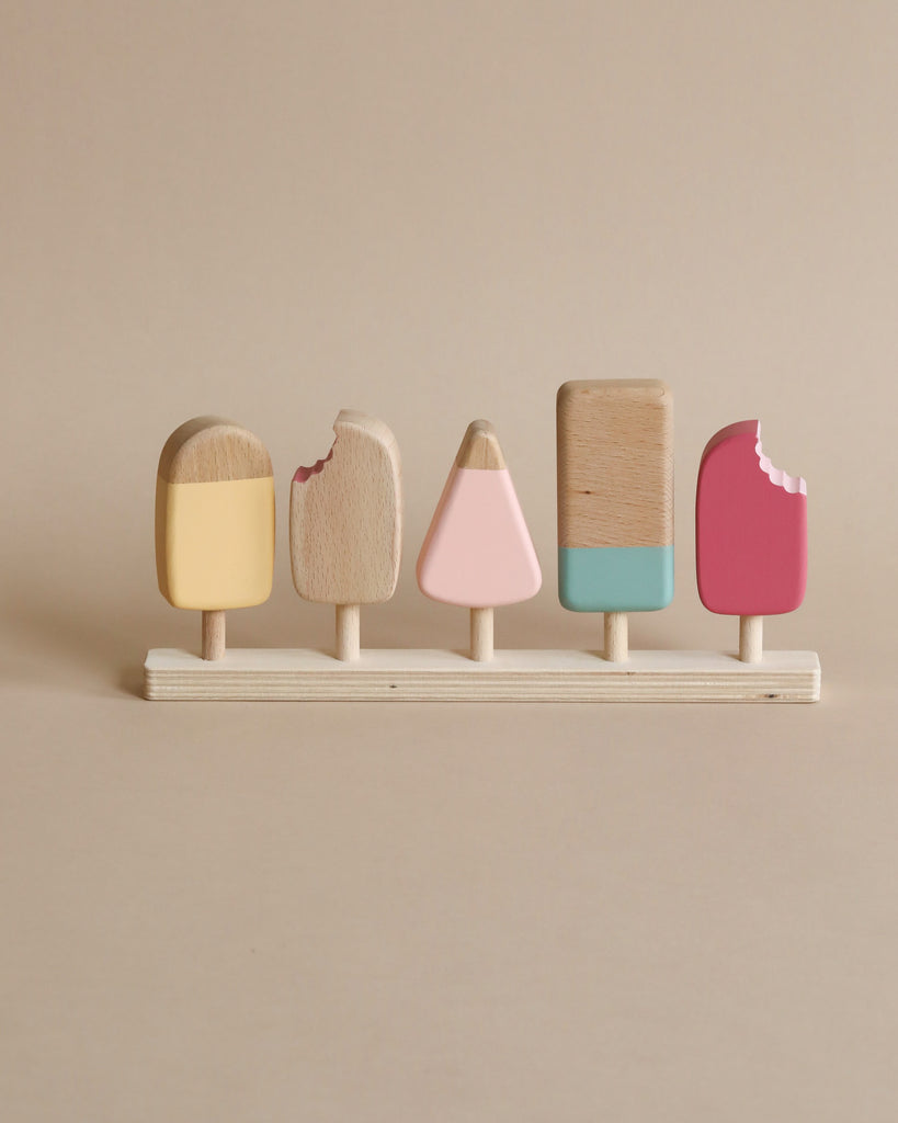 5 wooden popsicles on a stand in various popsicle shapes and in various pastel colors. 