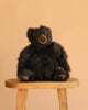A Brown Mikey Bear Stuffed Animal, 12", sits on a wooden stool against a plain beige background, showcasing its soft, realistic plush design.