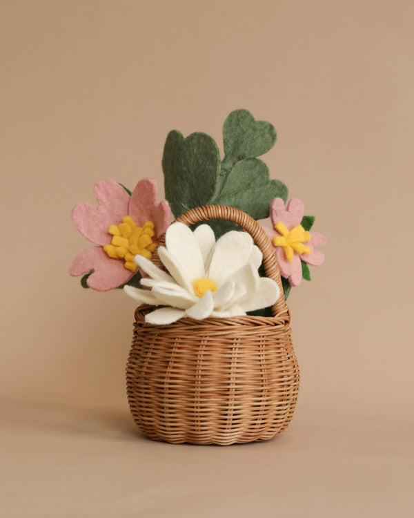 A Felt Flower Berry Basket filled with handmade flowers, including a prominent white flower in the center, surrounded by pink flowers and green leaves, against a beige backdrop.