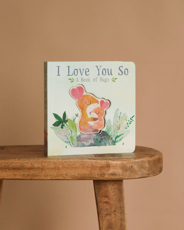 I Love You So by Patricia Hegarty" is a children’s interactive board book with two baby animals snuggling on the cover, shown upright on a wooden stool against a plain beige background.
