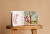 The open interactive board book "I Love You So" by Patricia Hegarty shows two pink baby animals near a tree on a wooden stool with the text: "Daddy looks on proudly as squirrel climbs a tree.