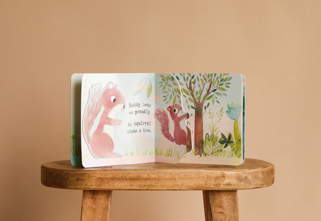 The open interactive board book "I Love You So" by Patricia Hegarty shows two pink baby animals near a tree on a wooden stool with the text: "Daddy looks on proudly as squirrel climbs a tree.