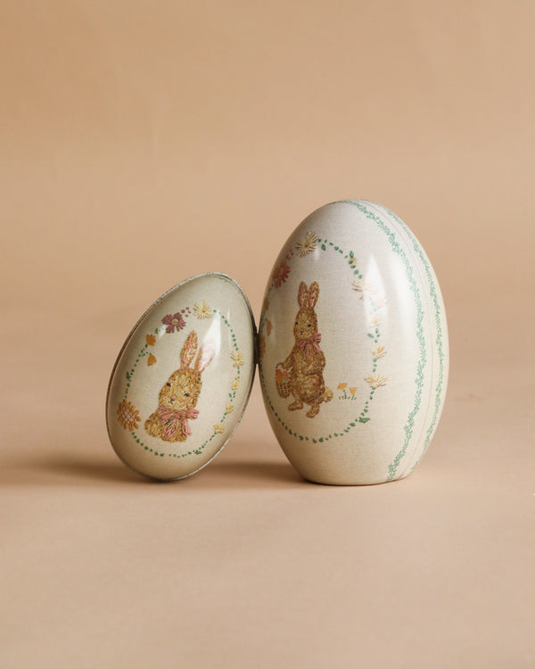 The Maileg Easter Egg - Set of Two - Pink features decorative eggs with vintage bunny and floral designs on a beige background. The larger egg stands upright while the smaller one leans against it, both with an embroidered look.