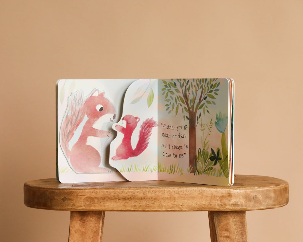 An opened copy of "I Love You So" by Patricia Hegarty rests on a wooden stool, displaying two illustrated baby animals, a tree, and the heartfelt text: "Whether you go near or far, you'll always be close to me.