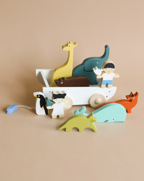 The Friend Ship Pull Toy depicting various animals and a figurine, arranged on a light brown background. This sustainable rubber wood set includes a giraffe, elephant, whale, penguin, fox, and more