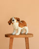 The Saint Bernard Puppy Dog Stuffed Animal, from our hand sewn plush animals collection, stands on a wooden stool against a plain peach background.