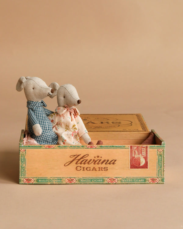 Maileg Grandma and Grandpa Mice in Cigarbox are seated inside their vintage wooden bed playset against a beige background.