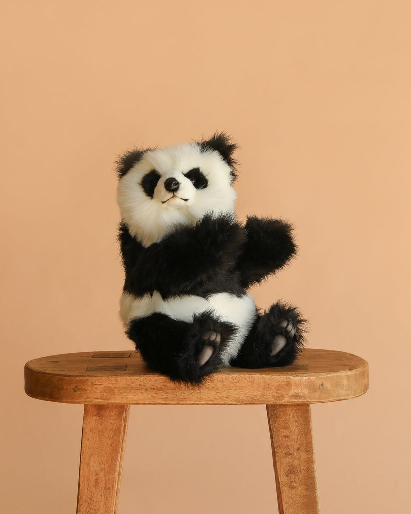 The Panda Cub Stuffed Animal, featuring soft black and white fur, sits upright on a wooden stool with a plain beige background.