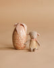 A small plush mouse with a pink ribbon sits beside the Maileg Easter Egg with Lamb & Extra Clothing—an egg-shaped box with floral patterns and a fabric bow—both set against a neutral beige background.