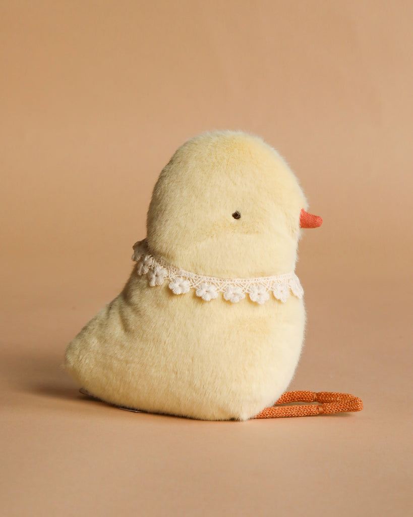 A plush yellow chick toy with an orange beak and feet, wearing a white lace collar, sits on a beige surface beside the Maileg Easter Basket Set against a matching beige background.