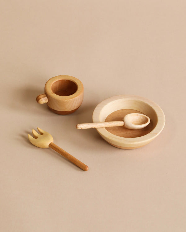 A Handmade Pretend Dinnerware Set, fork, spoon, and bowl arranged neatly on a beige background. The bowl contains a small wooden spoon, and all items exhibit a natural wood finish. This set of handmade wooden cut