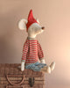 The Maileg Christmas Maxi Mouse, dressed in a cozy red and white striped sweater, blue pants, and a festive Christmas hat, is seated on a closed wicker basket against a beige background.