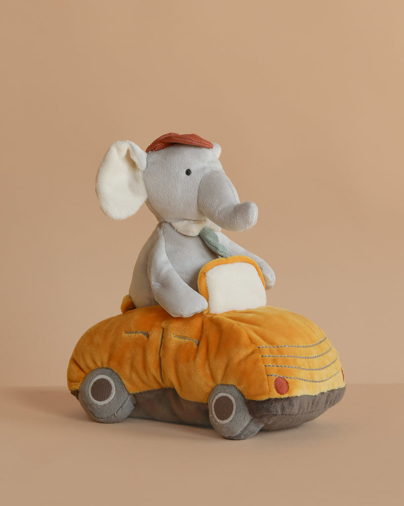 The Elephant Driver Plush Toy features a plush elephant with a brown hat and green tie sitting on a stuffed car, creating an adorable two-in-one plushie displayed against a plain beige background.