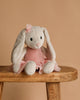 The Steiff Hoppie Rabbit Ballet, dressed in a pink tutu and bow, sits on a wooden bench against a beige background.