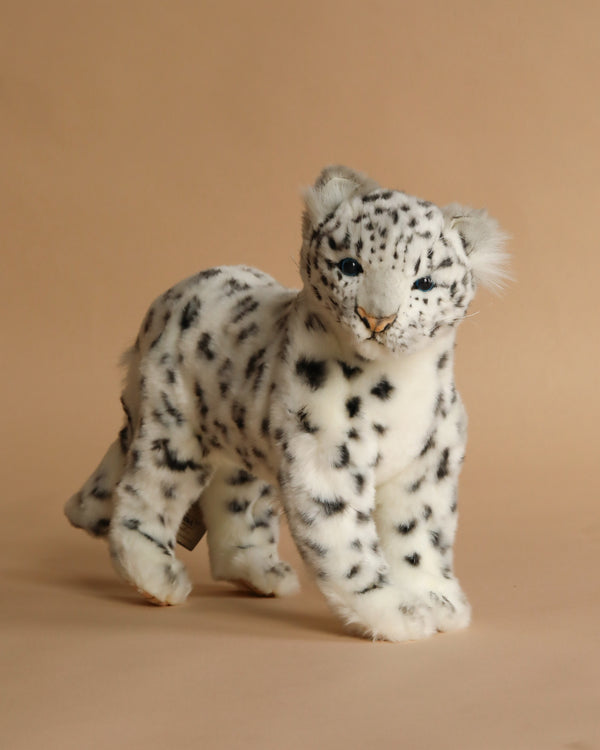The Snow Leopard Standing Stuffed Animal features soft white fur with black spots, blue eyes, and a realistic look. Perfect for fans of lifelike plush toys, it stands on a light beige background.