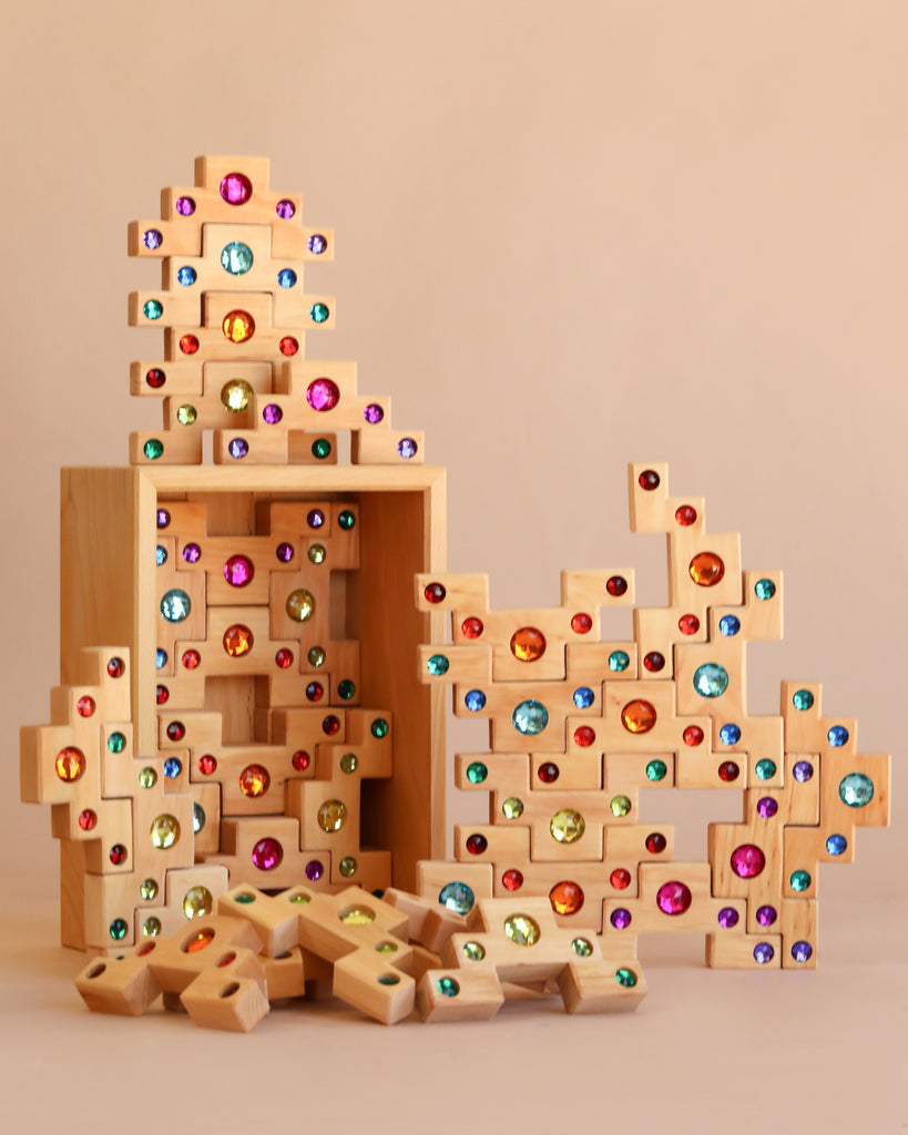 The Bauspiel Colored Stair Blocks - 40 Piece set features vibrant, gem-like wooden blocks stacked in imaginative shapes, with some creative structures built while other pieces are scattered on a neutral background.