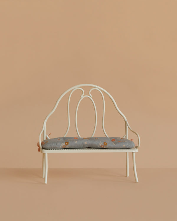 The Maileg Vintage Bench, Miniature - Off White features a decorative backrest and a light blue floral cushion, ideal for displaying Maileg bunnies or teddy bears against any background.