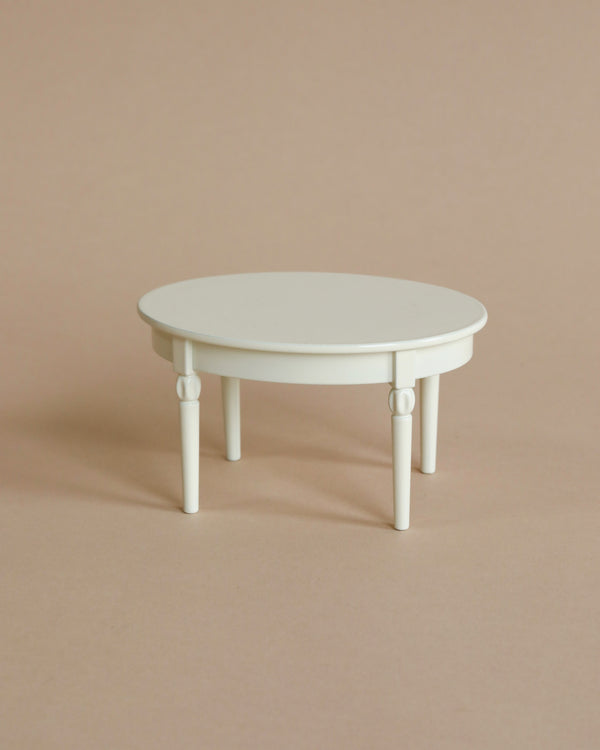 A simple, small, white circular Maileg Miniature Dining Table with four legs, set against a plain light beige background.