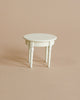 A small, white, round Maileg | Mini Side Table with three legs, photographed against a plain beige background. The table has simple, elegant design elements on its legs.
