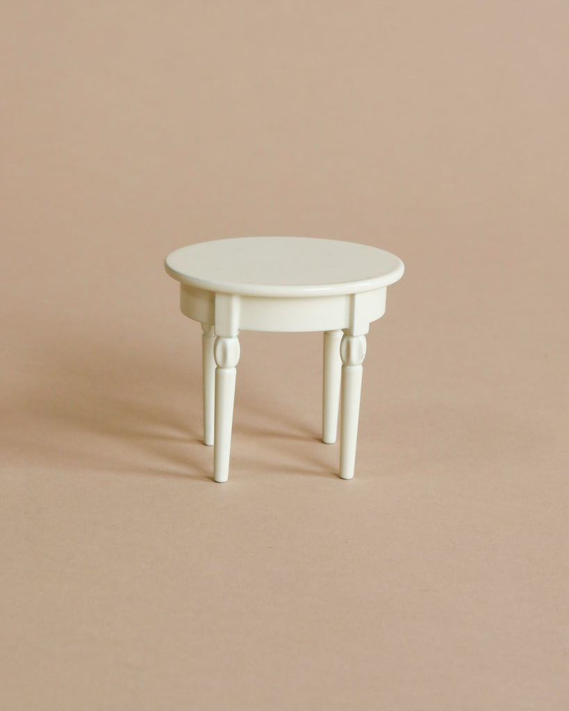 A small, round, white table with three legs sits on a beige background, ideal for showcasing your Maileg Pastry Chef Set With Grapat Wooden Bake Set.