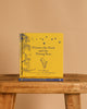 A yellow hardcover of "Winnie-the-Pooh: Winnie-the-Pooh and the Wrong Bees" stands upright on a wooden bench, featuring classic children’s story illustrations of Pooh, bees, and a tree, with another copy placed below it.