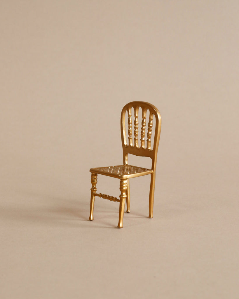 A small, gold-colored decorative chair with a spindled backrest and patterned seat is centered against a plain beige background—ideal for the Maileg Family Theater Set or displaying Maileg mice accessories.