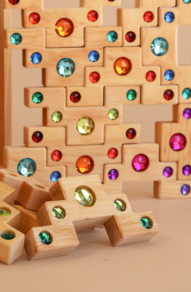 The Bauspiel Colored Stair Blocks - 40 Piece set features vibrant wooden blocks with colorful gem-like stones embedded, stacked and scattered to create a playful, eye-catching display.