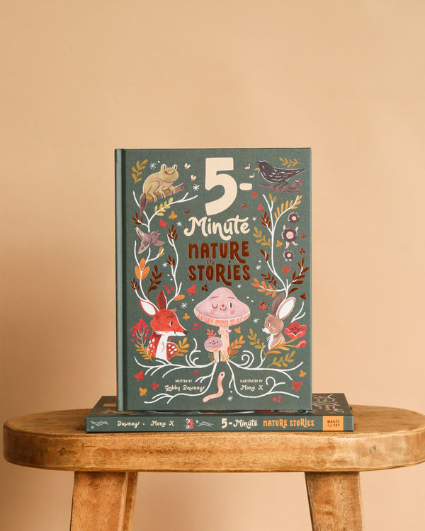 The hardcover "5-Minute Nature Stories" stands upright on a wooden stool, its cover featuring colorful woodland animals and plants, with another copy lying flat beneath it.